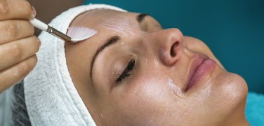 A medical provider uses a brush to apply a chemical peel on a woman's face
