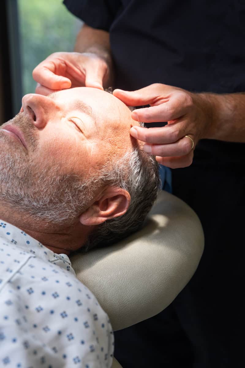 A man getting a medical procedure has a bandage placed on his forehead by a dermatologist